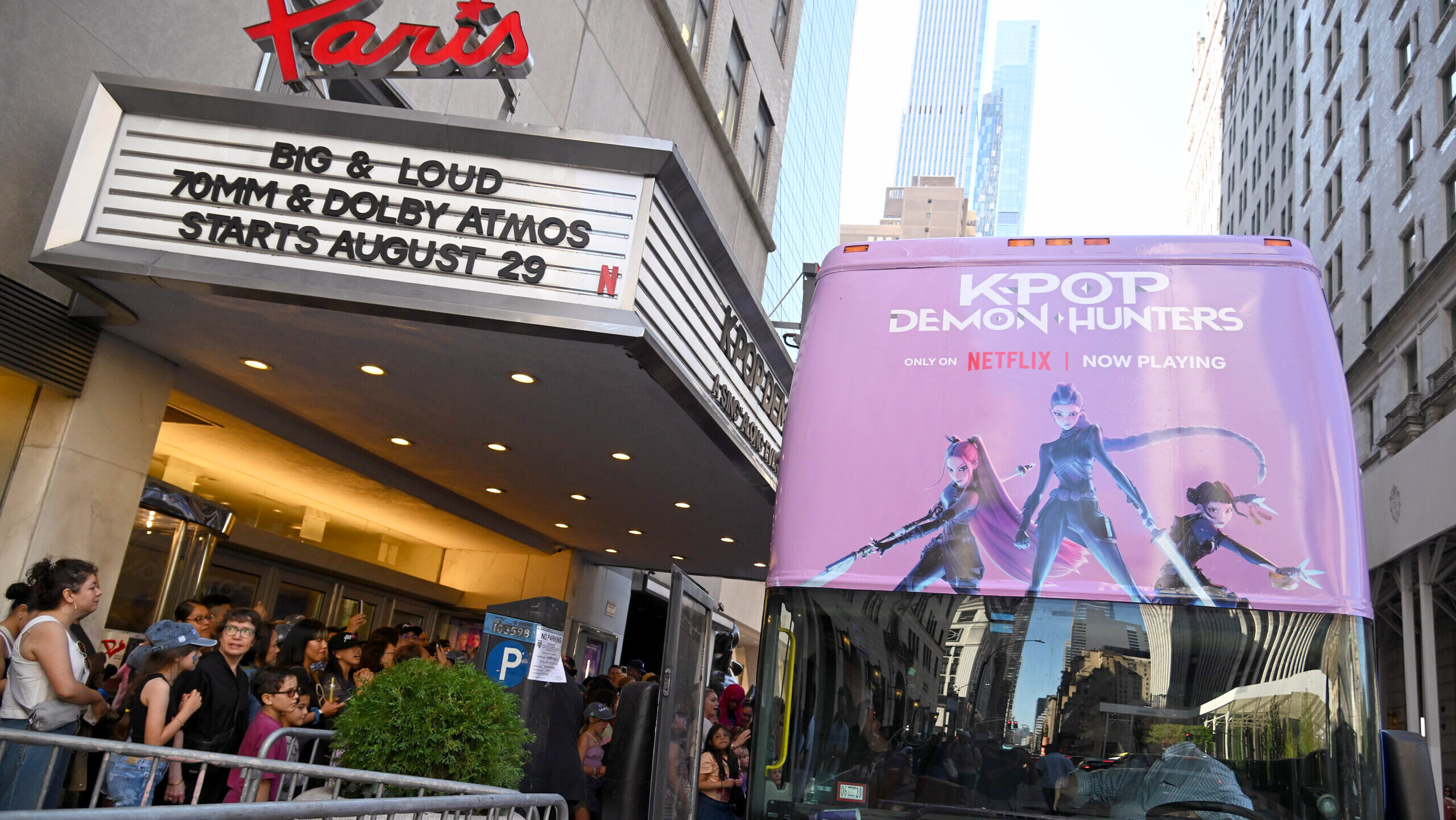 A bus featuring a KPop Demon Hunters advertisement on it is seen parked outside a cinema in New York City.