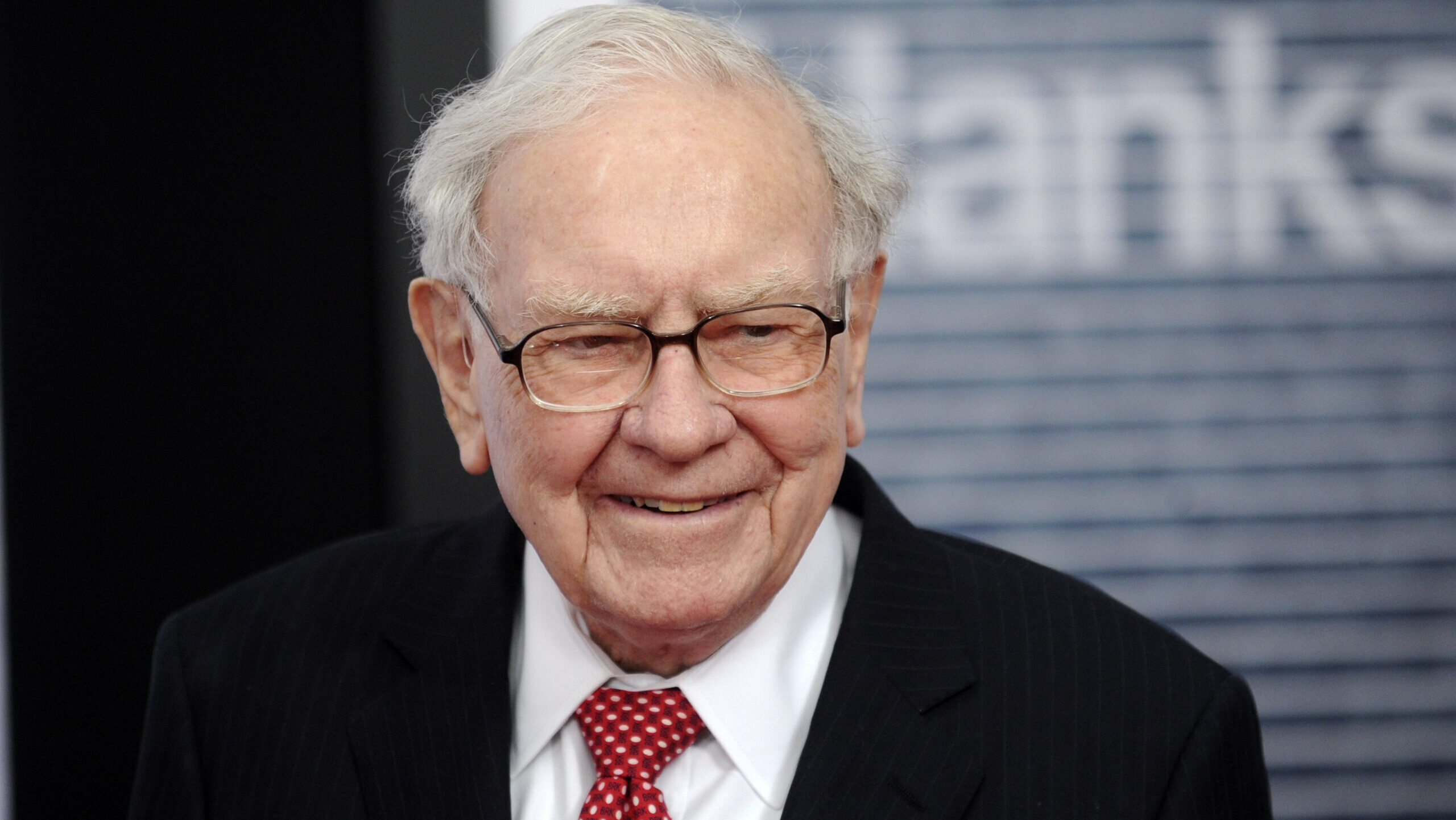Warren Buffett, wearing a striped black suit jacket and a red tie, is seen smiling at the Newseum in Washington, D.C.