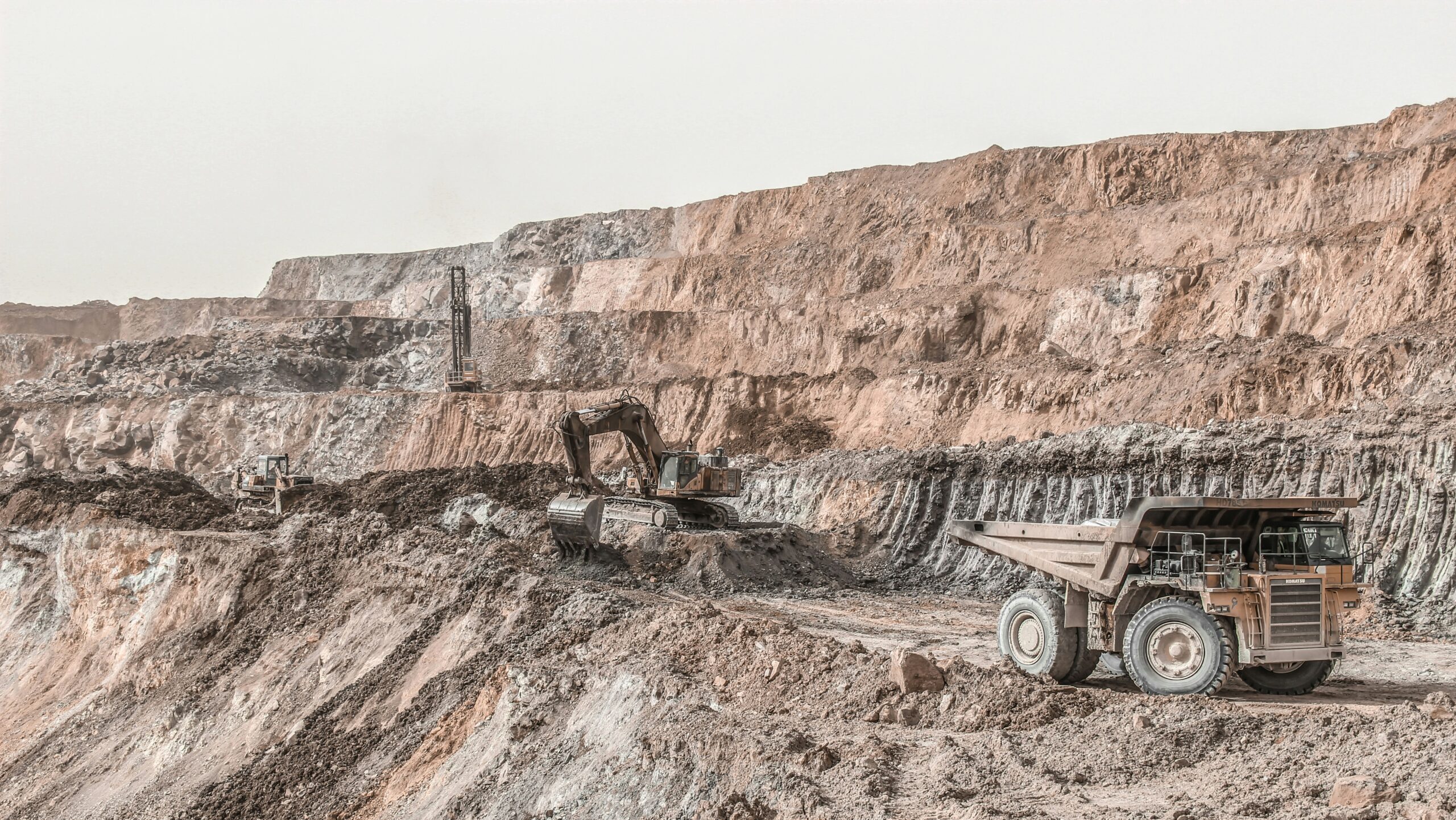 Multiple large mining vehicles are shown working a copper mine along a series of rocky cliffs.