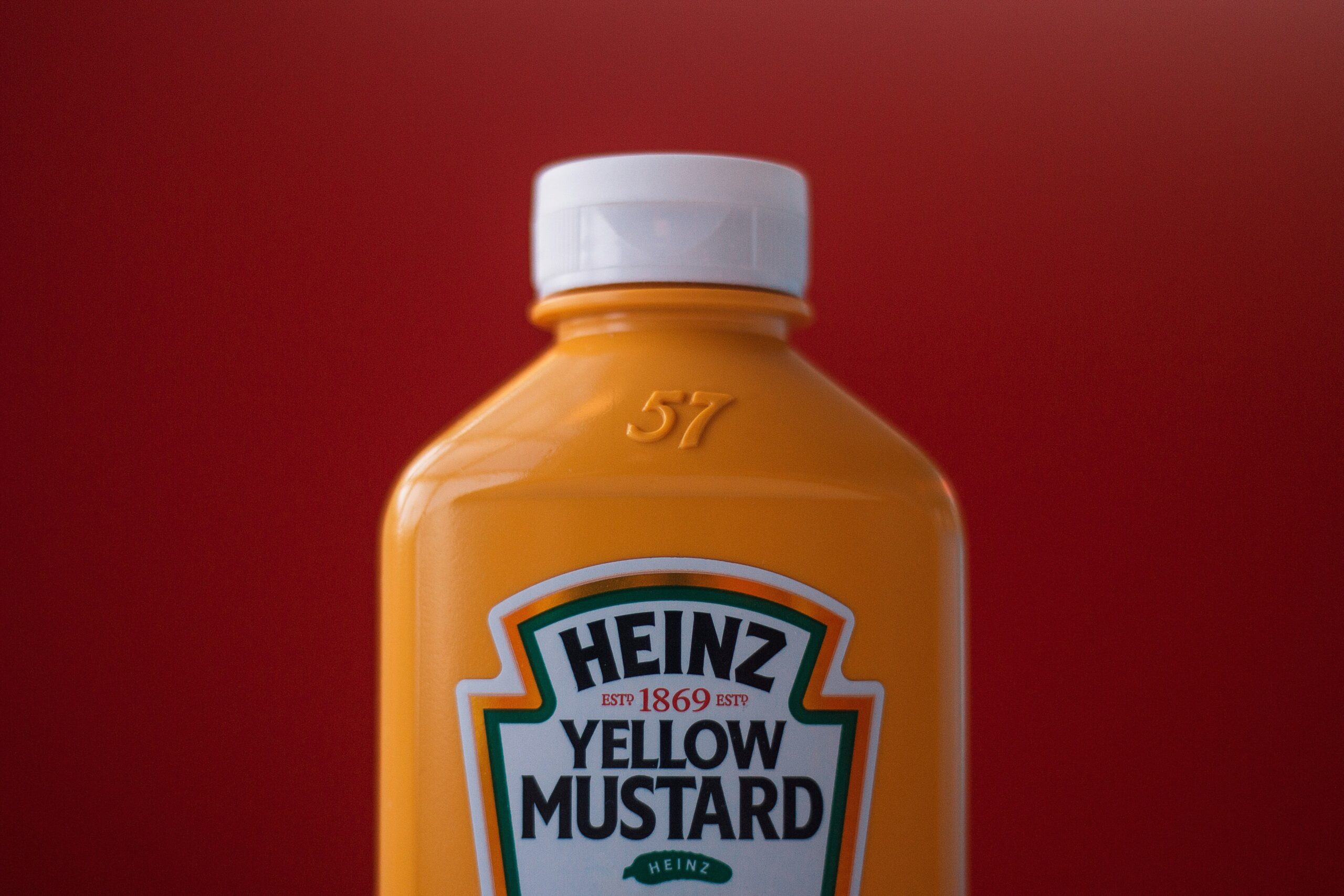 A bright yellow plastic container of Heinz mustard is shown in front of a bright red background.