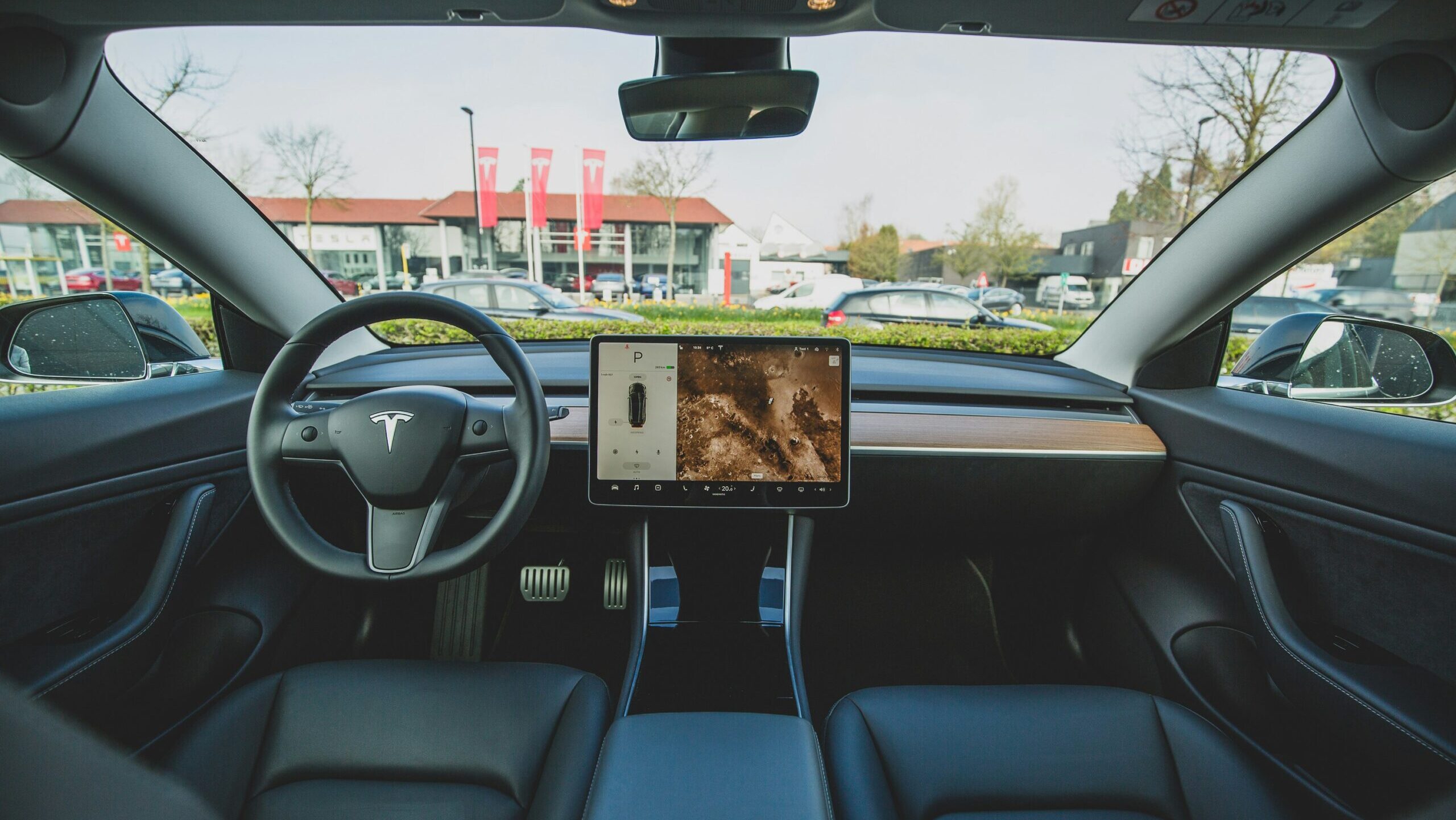 A view from inside a Tesla car looks out onto one of the company's dealerships, where flags with the Tesla logo hang.