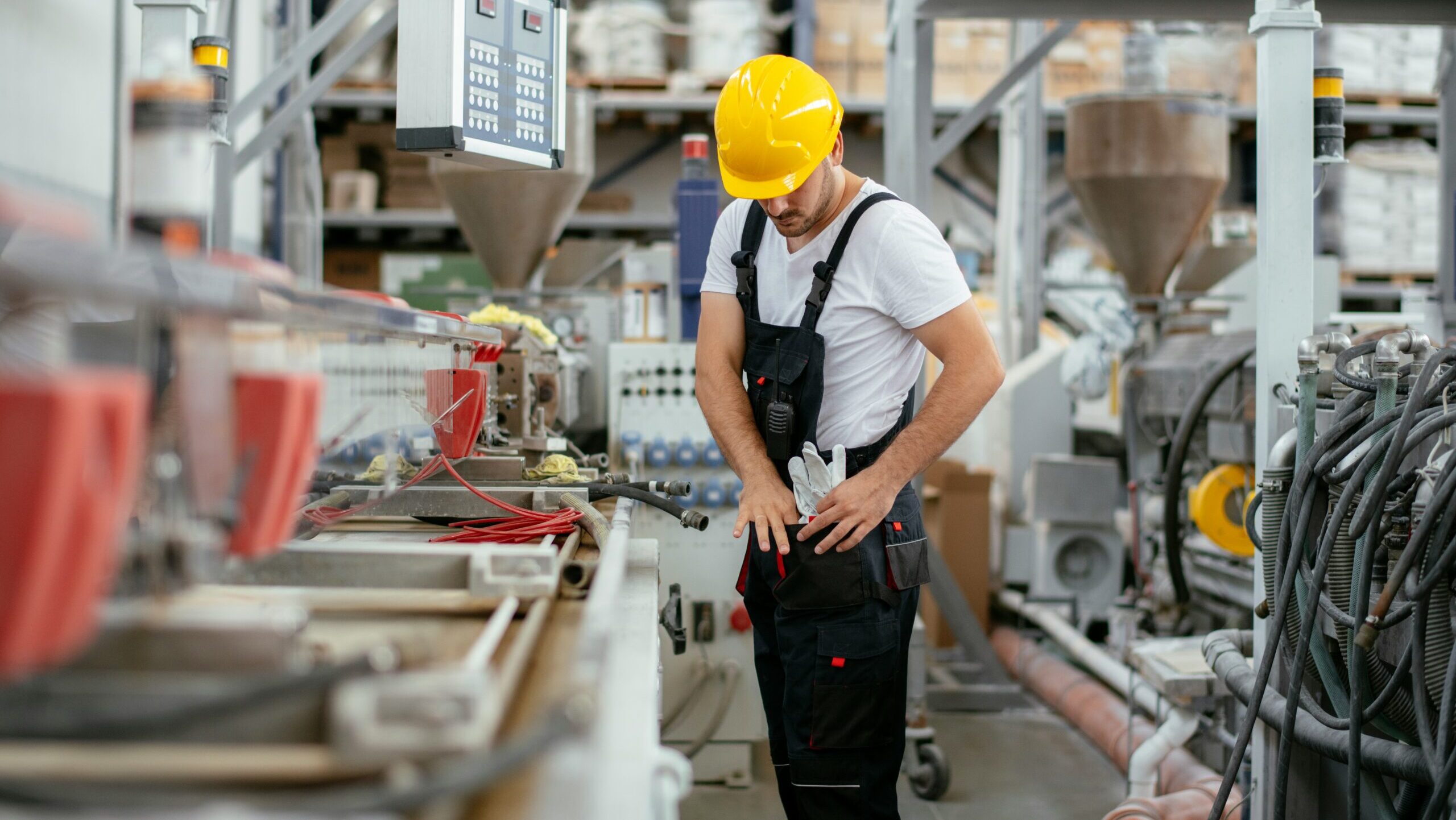 A factory worker adjusts his gloves in a utility pouch at his waist.