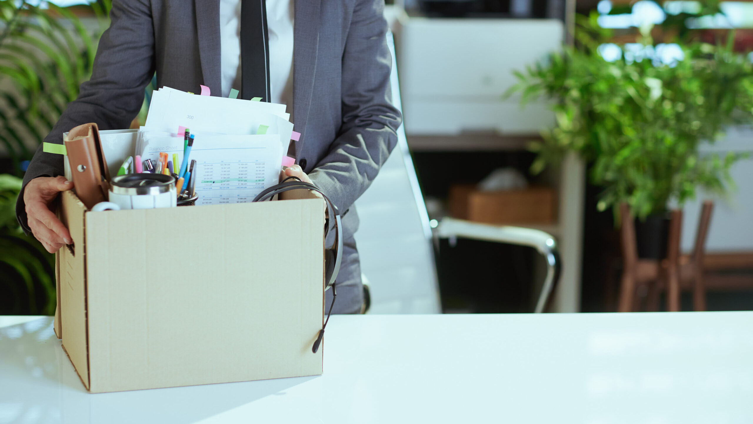 An employee is shown with their belongings collected in a cardboard box on their desk, indicating they may have been laid off.