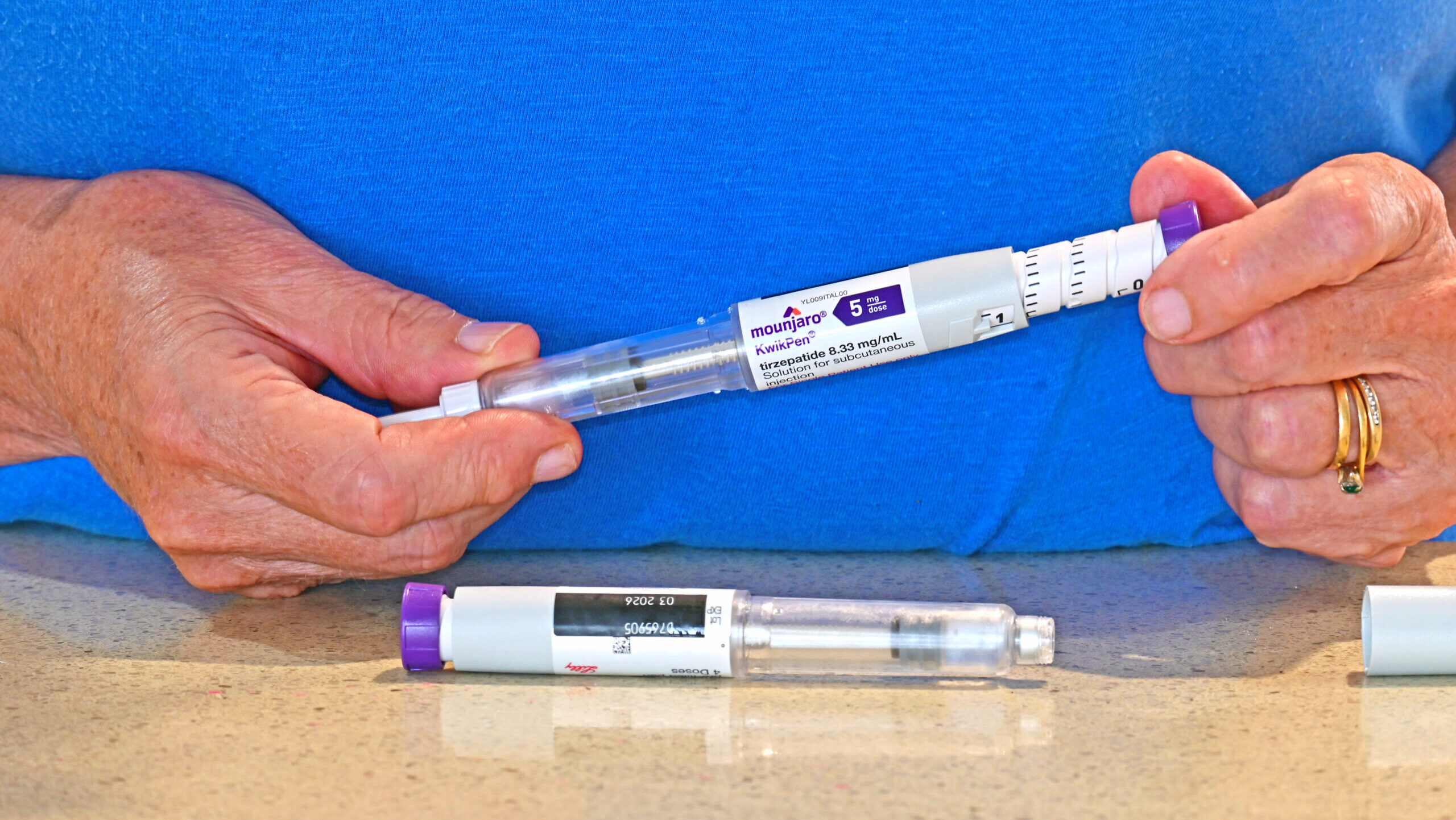 A person's hands are shown handling a does of GLPT-1 drug Mounjaro, which is manufactured by Eli Lilly