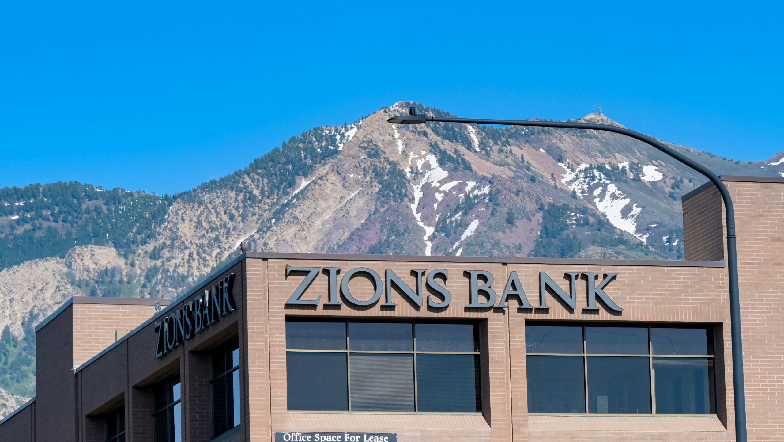 An exterior view of a Zions Bank location in the centre of Ogden, Utah with a tall snow-capped mountain in the background.