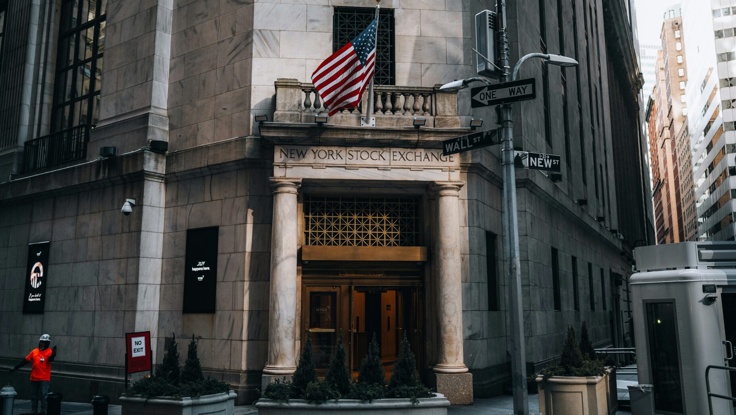 An entrance to the New York Stock Exchange on New York City's Wall Street is shown, with a US flag above the doors.