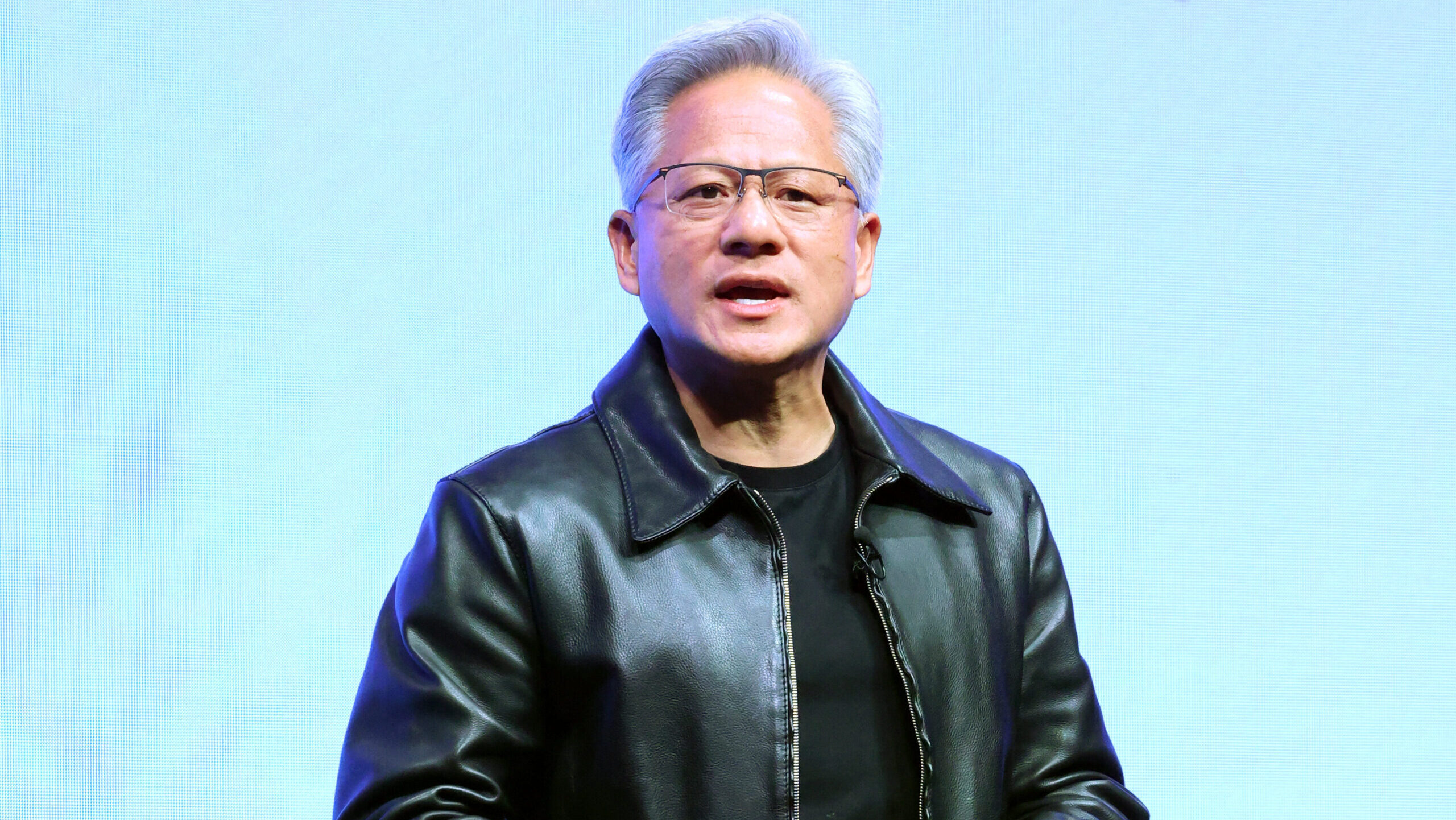 Nvidia CEO Jensen Huang, wearing his trademark black leather jacket, is seen addressing a crowd on stage.