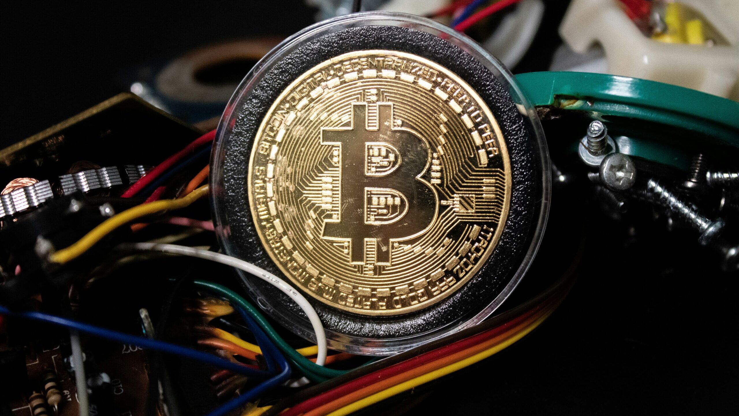 A coin bearing the Bitcoin logo if shown positioned on top of technical wiring and gear.