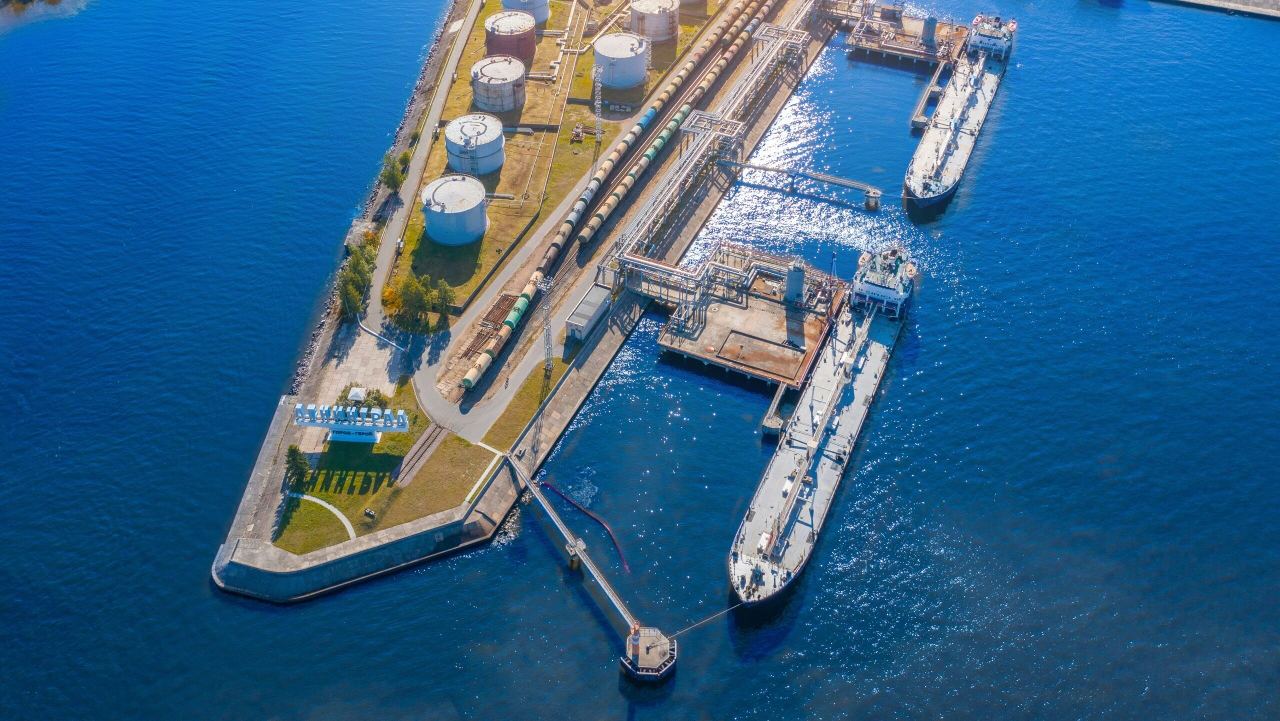 Ships are shown docked at a harbor with an oil refinery and rail depot.