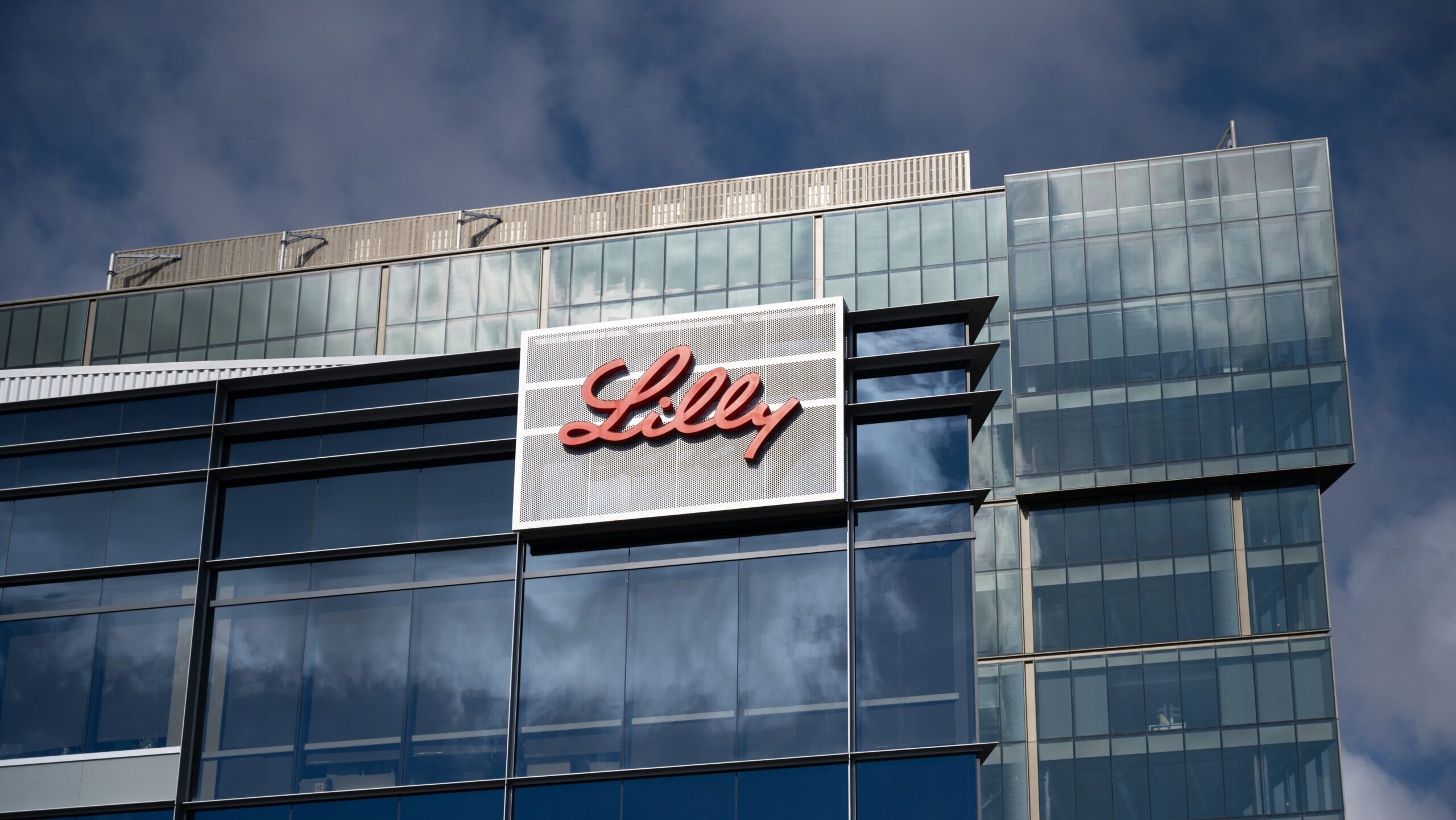 The Eli Lilly logo is shown on a glass office building facade.
