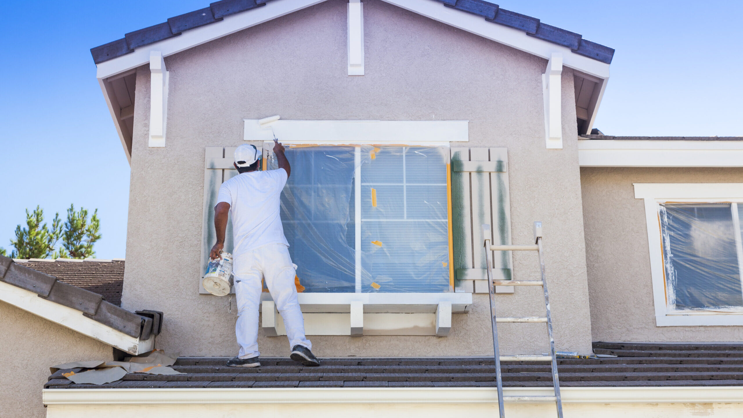 A painter works on the trim and shutters of a home window.