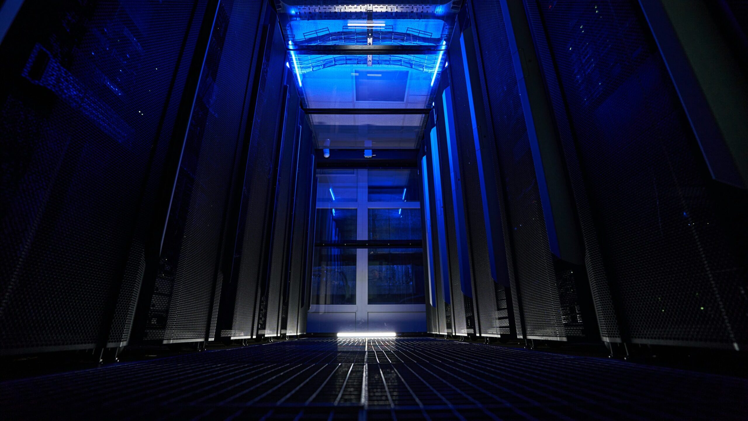 A lowly lit server room inside a data center is shown with racks of data storage hardware in metal cabinets.