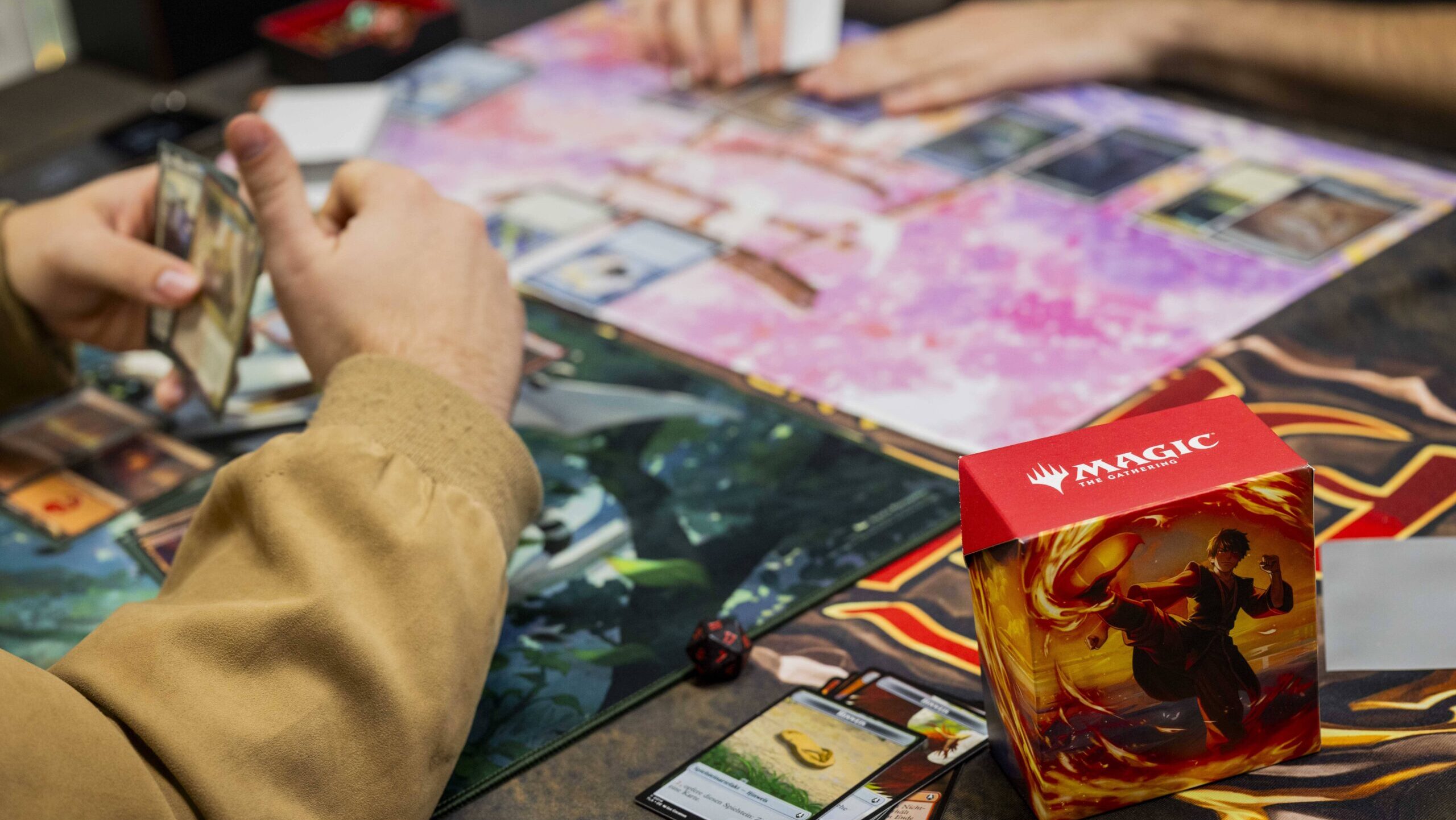 Two players, their hands shown at a Magic: the Gathering board, play the strategy game against one another.