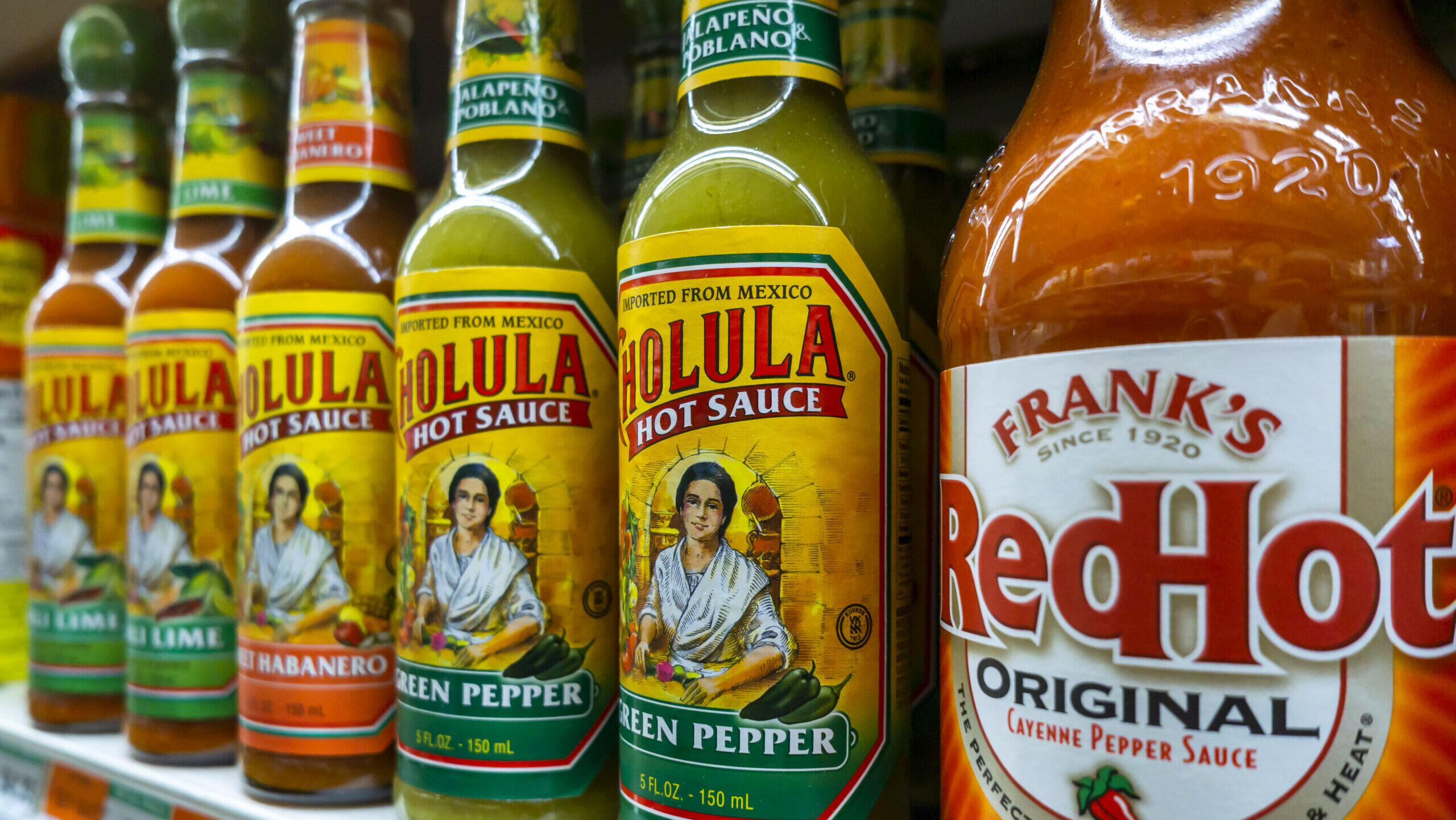 Photo of bottles of Cholula and Frank's RedHot hot sauce on supermarket shelves.