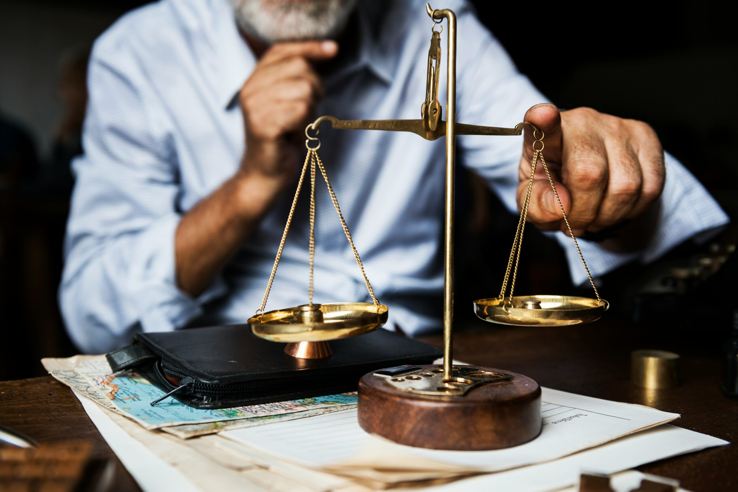 Photo of man sitting at desk putting his finger on a balance scale.