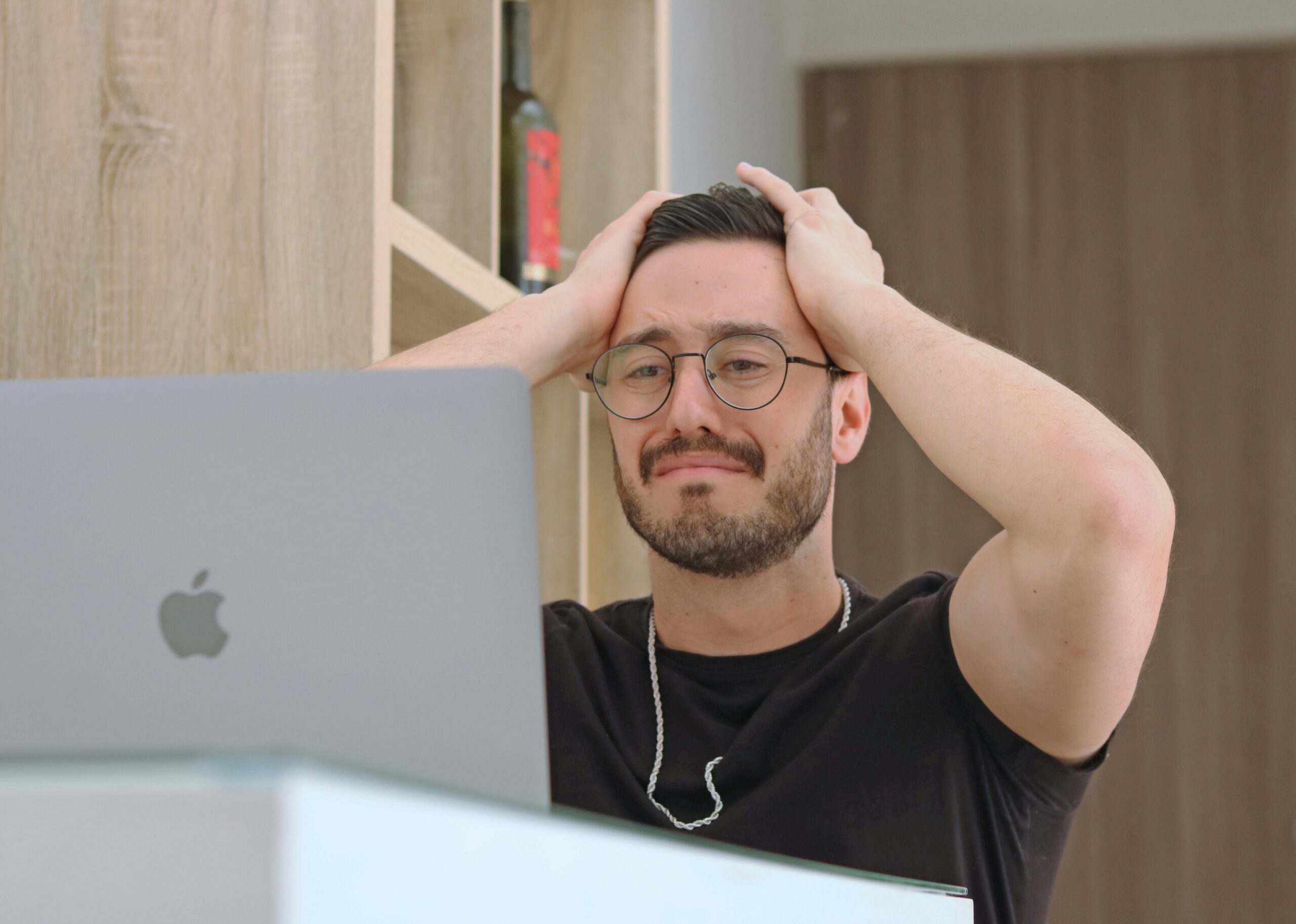 Photo of man looking disappointed while looking at a computer with his hands on his head.