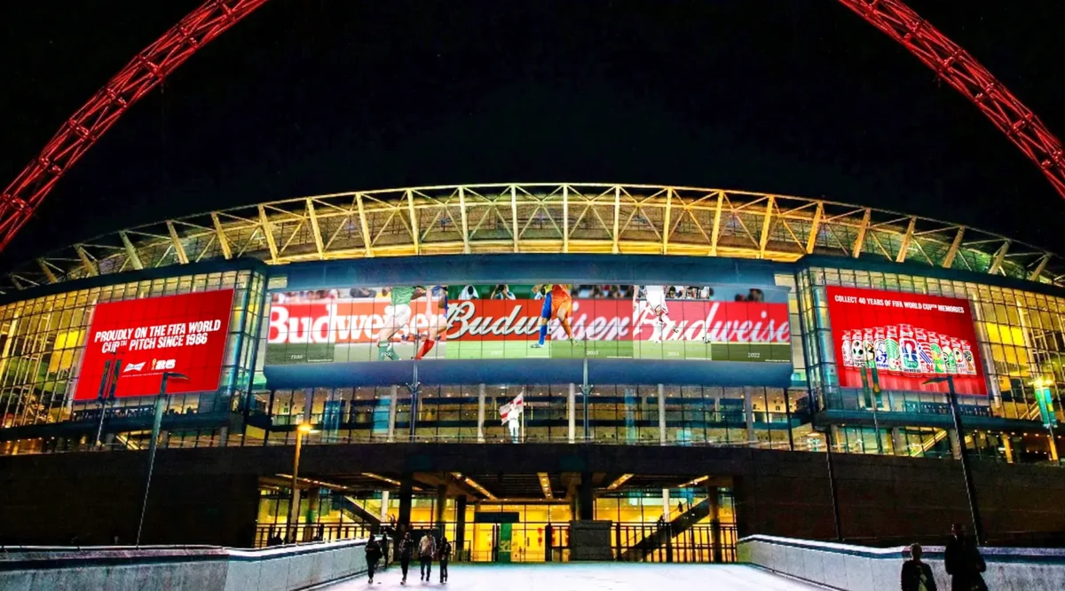 Budweiser soccer adverts are shown on the front of a stadium at night.