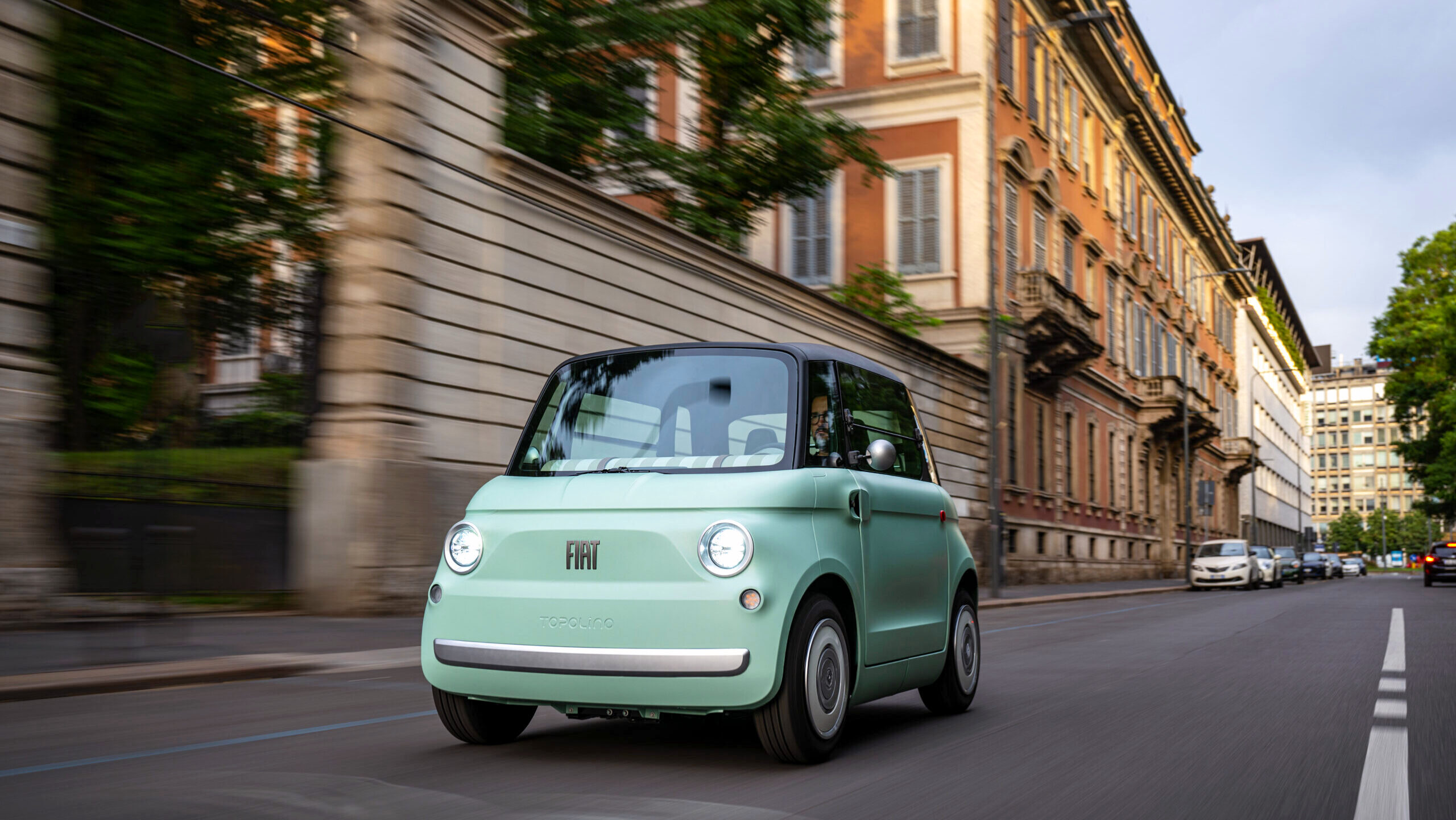 A Fiat Topolino car is shown driving down a residential street.