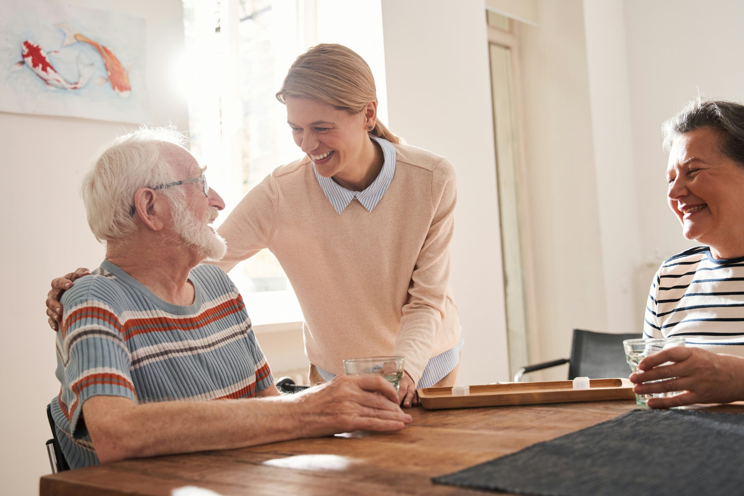 Photo of an older man sitting at a table while talking with two women.