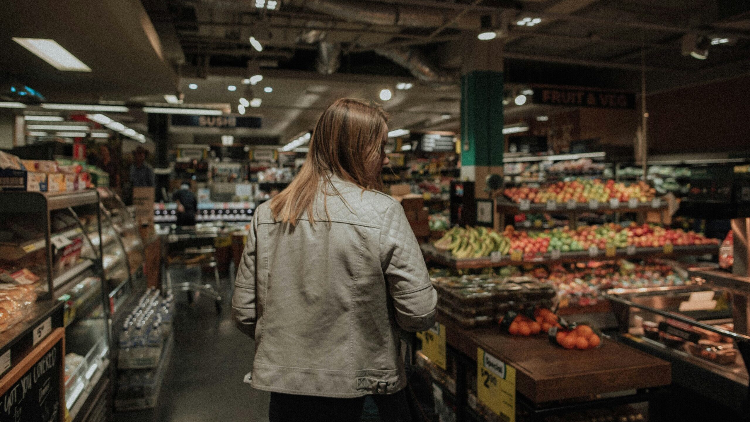 A woman navigates in front of the fruit and vegetable section at a grocery store.