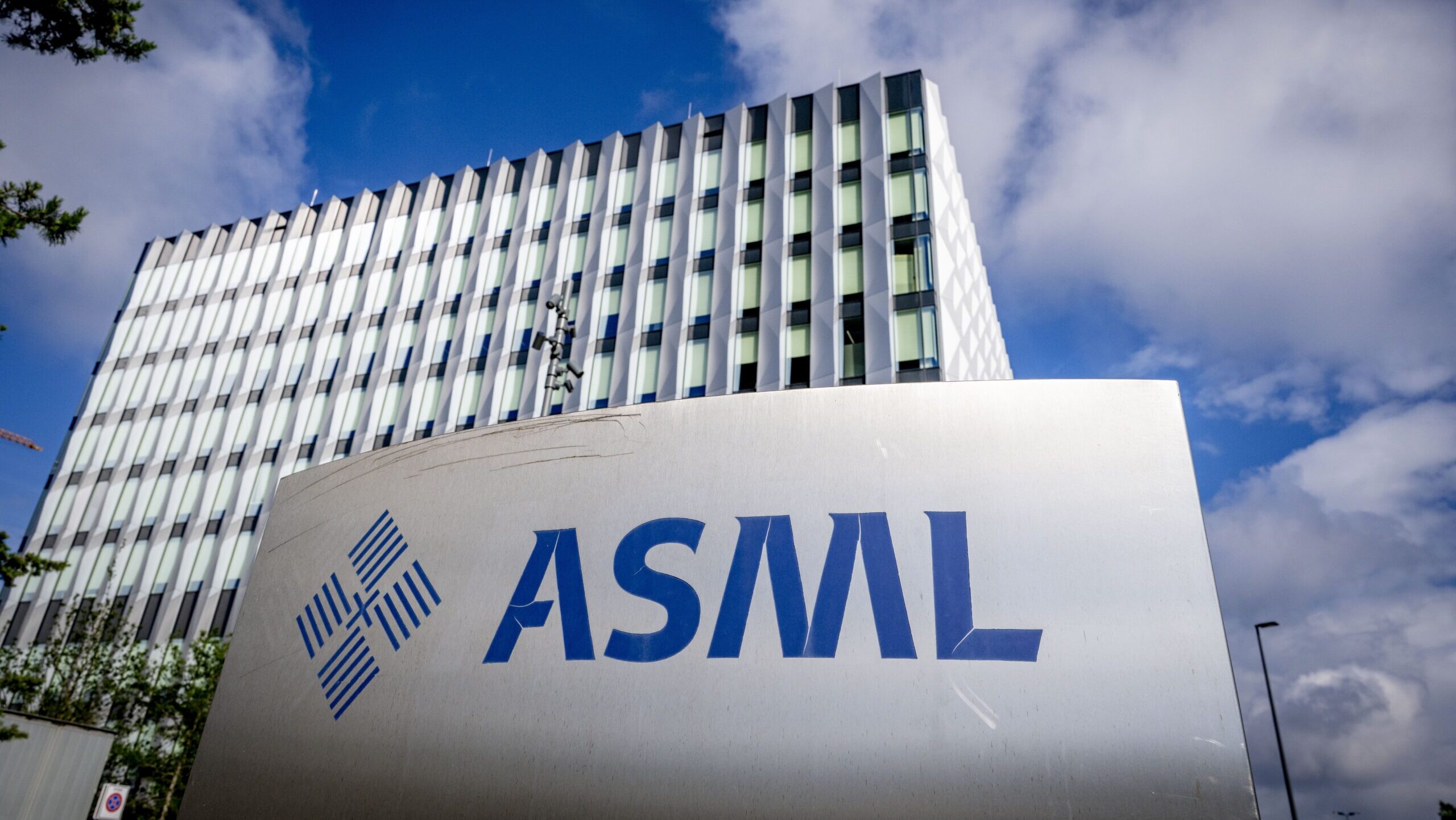 ASML's headquarters in the Dutch town of Veldhoven is shown in front of a bright blue and cloudy sky.