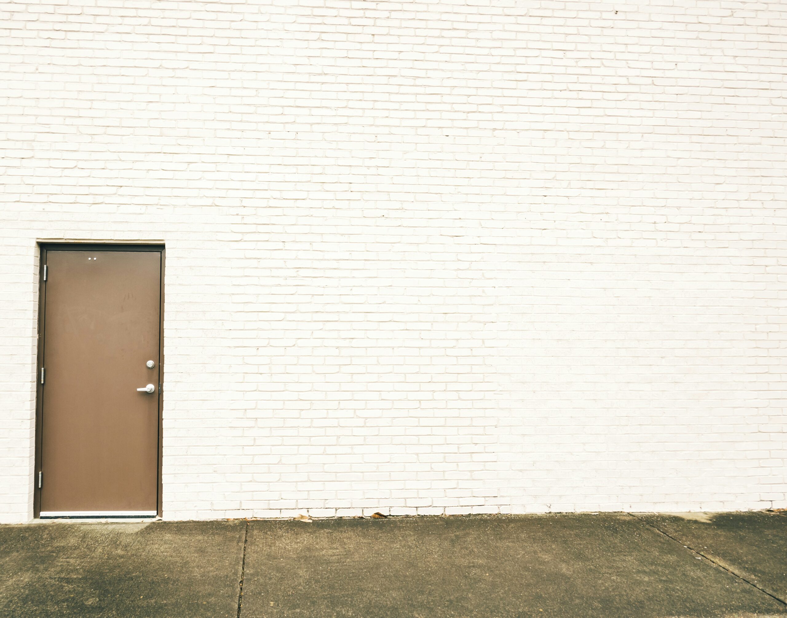 Photo of a brown door in a white brick wall.
