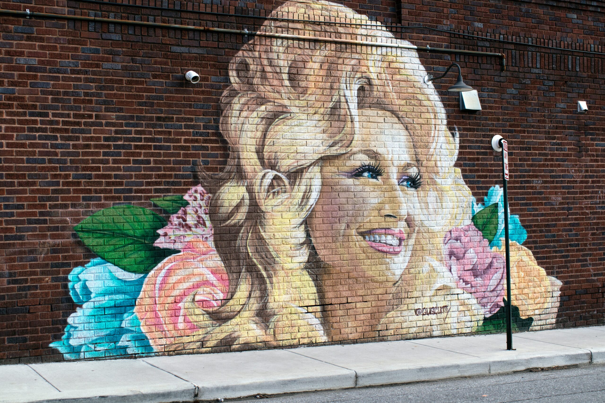 Photo of a painted mural of Dolly Parton on a red brick wall.